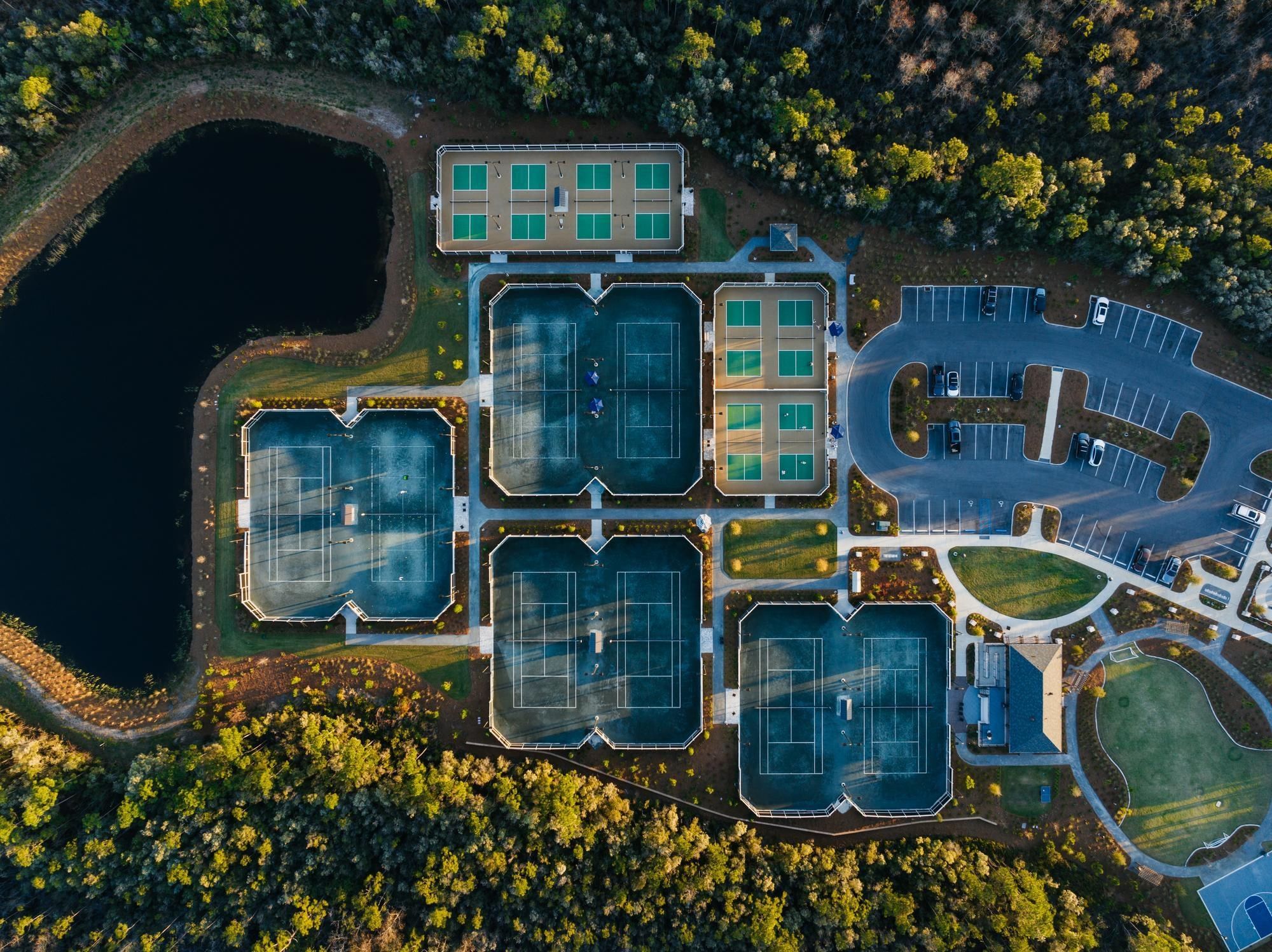 Aerial view of tennis courts, parking, and a lake at Watersound Inn
