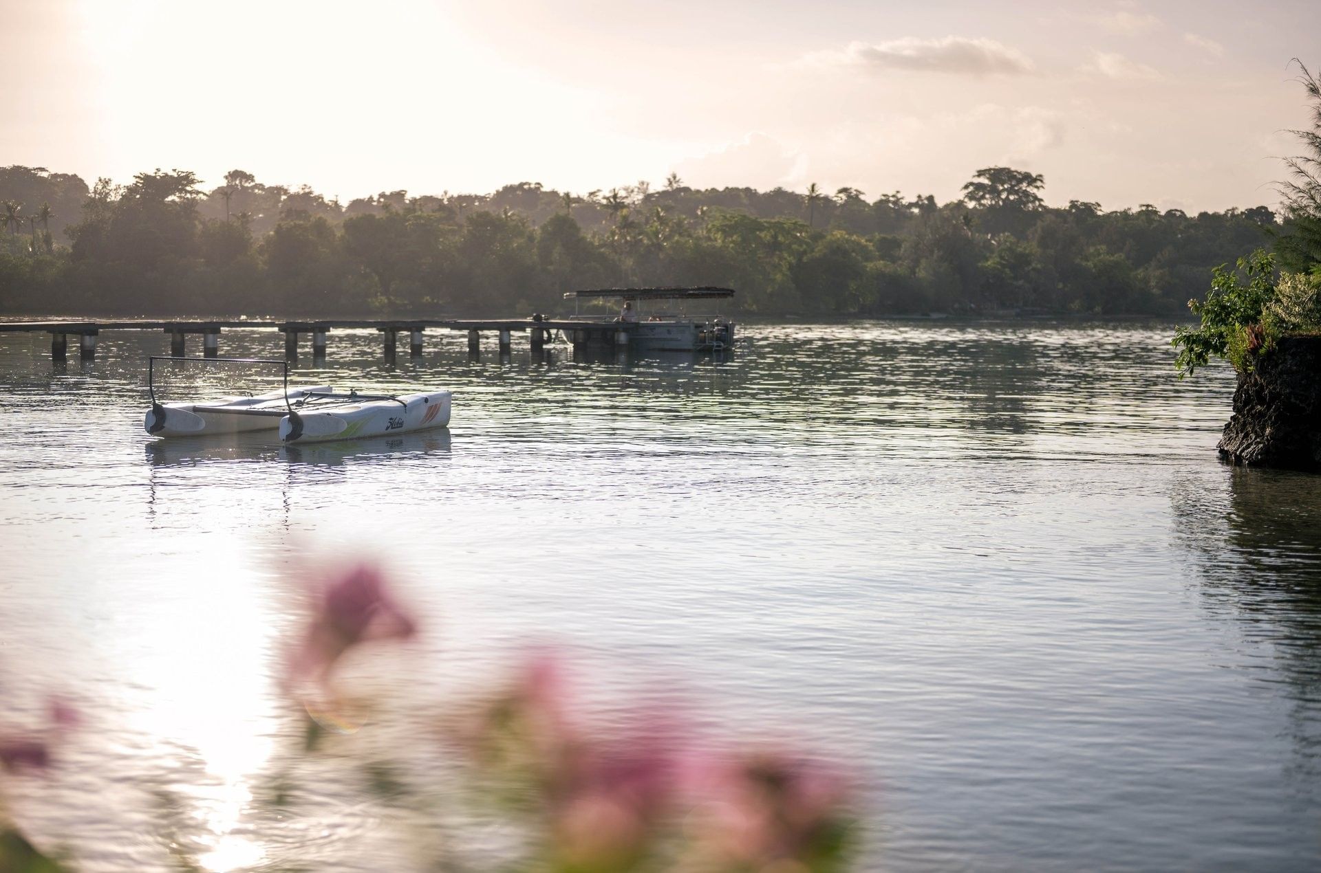 peaceful lake at sunset with a small catamaran floating near a wooden pier and forest at Warwick Le Lagon - Vanuatu