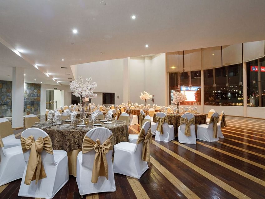 Bice event space with banquet tables, gold-bowed chairs, and floral centerpieces for a party at Real Inn Tijuana