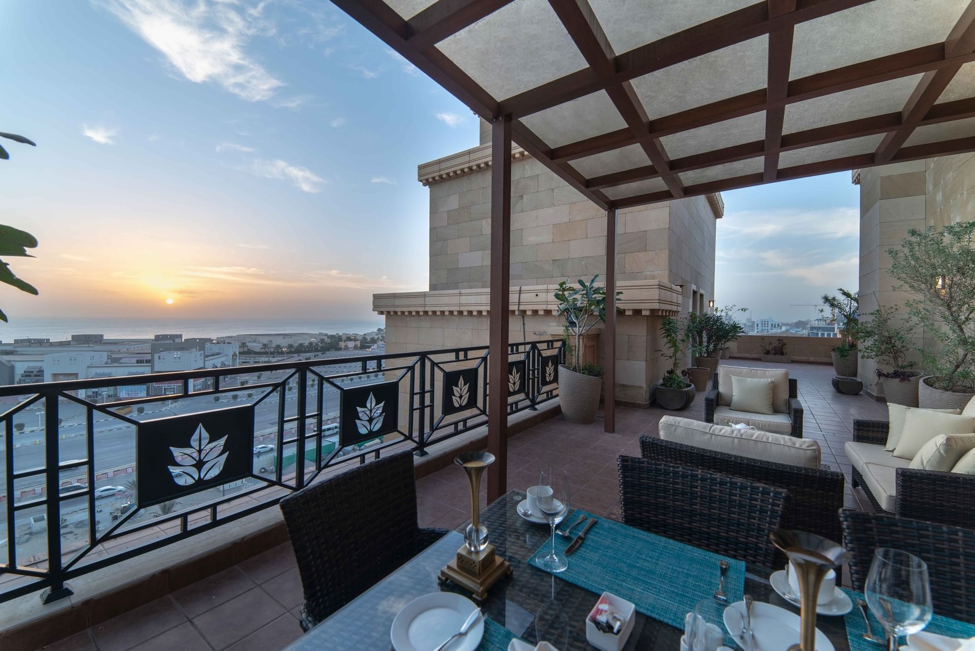 Outdoor dining table by wicker lounge chairs under a wooden pergola in Penthouse Villa at Warwick Al Khobar