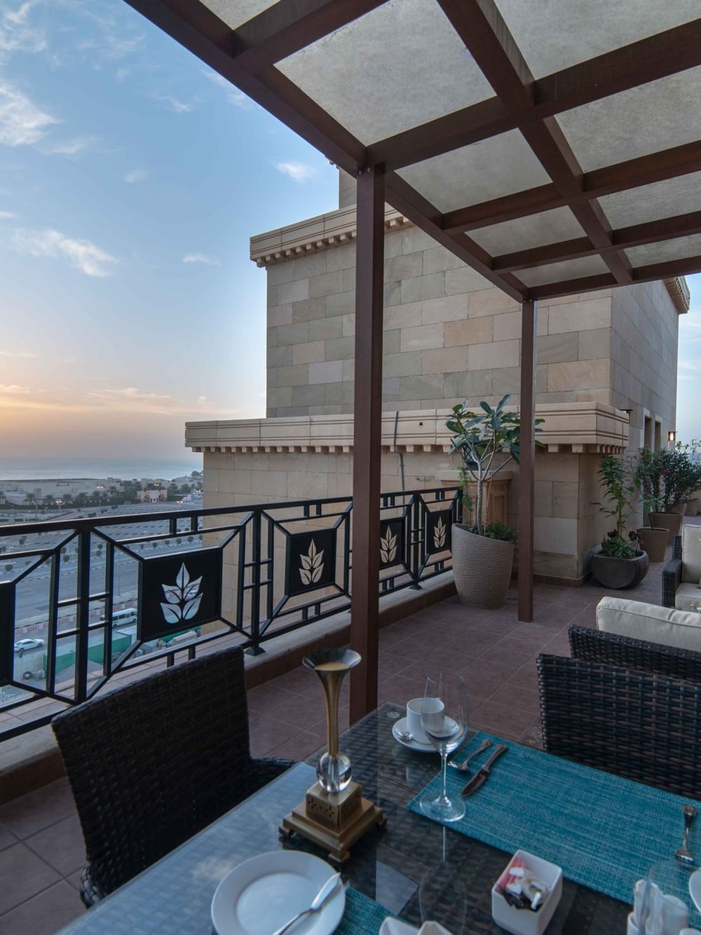 Outdoor dining table by wicker lounge chairs under a wooden pergola in Penthouse Villa at Warwick Al Khobar