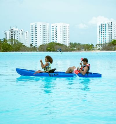 Two guests kayaking in turquoise waters with white resort buildings in the background at Playa Blanca Beach Resort