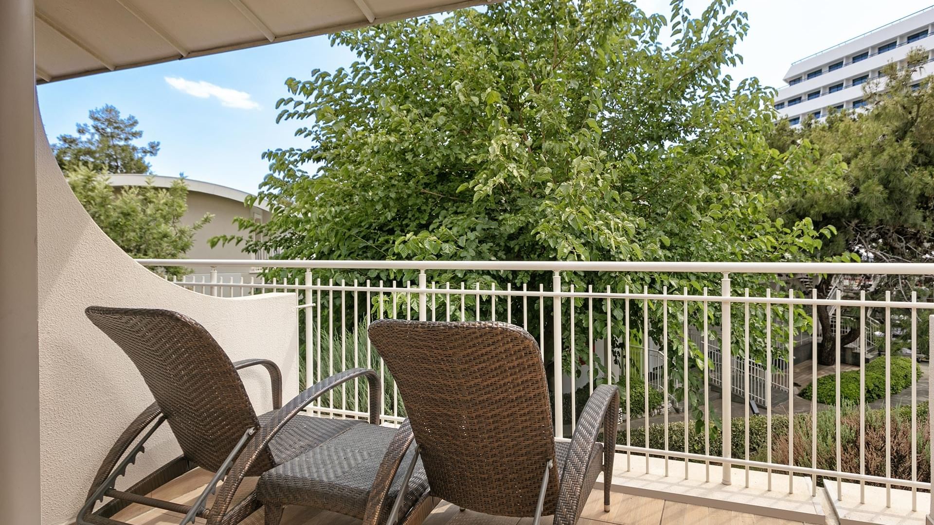 Wicker chairs and a stylish coffee table on a greenery-view balcony at Titanic Deluxe Lara.
