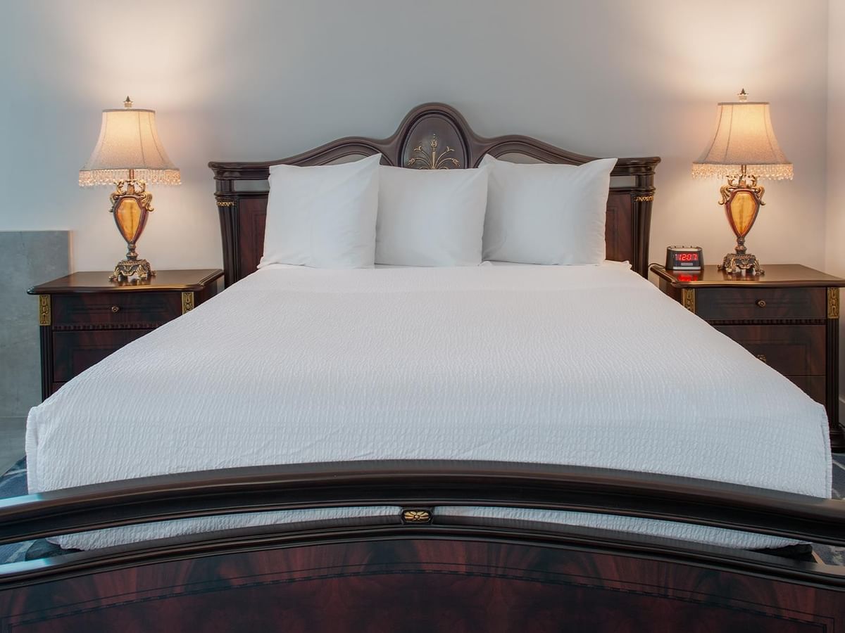 Hotel suite with white bedding, wooden nightstands, and lamps.