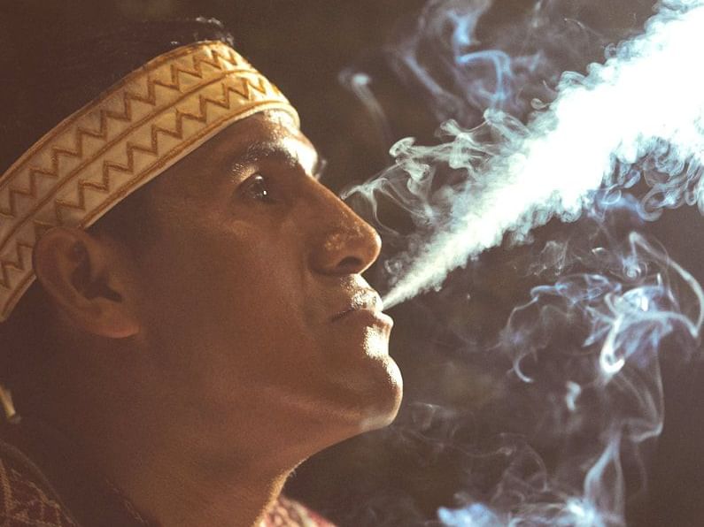 A person in a traditional outfit blowing smoke from his mouth 
