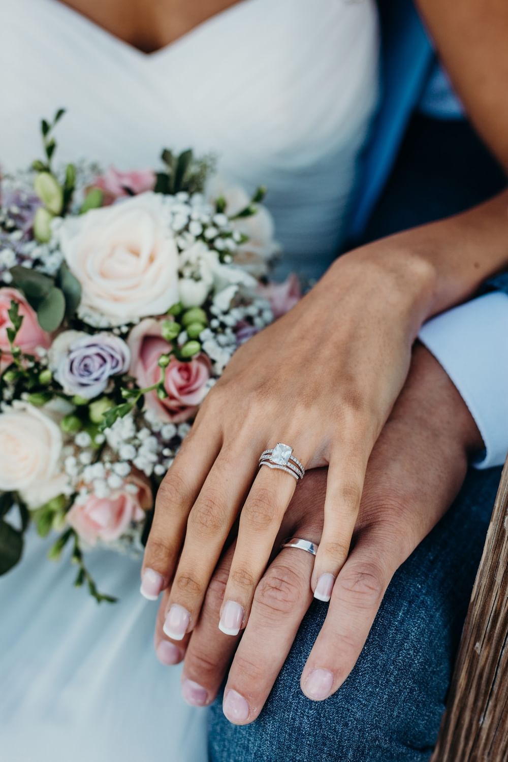Hands of a bride and groom with rings by a bouquet of pink and white roses, at Warwick Seattle