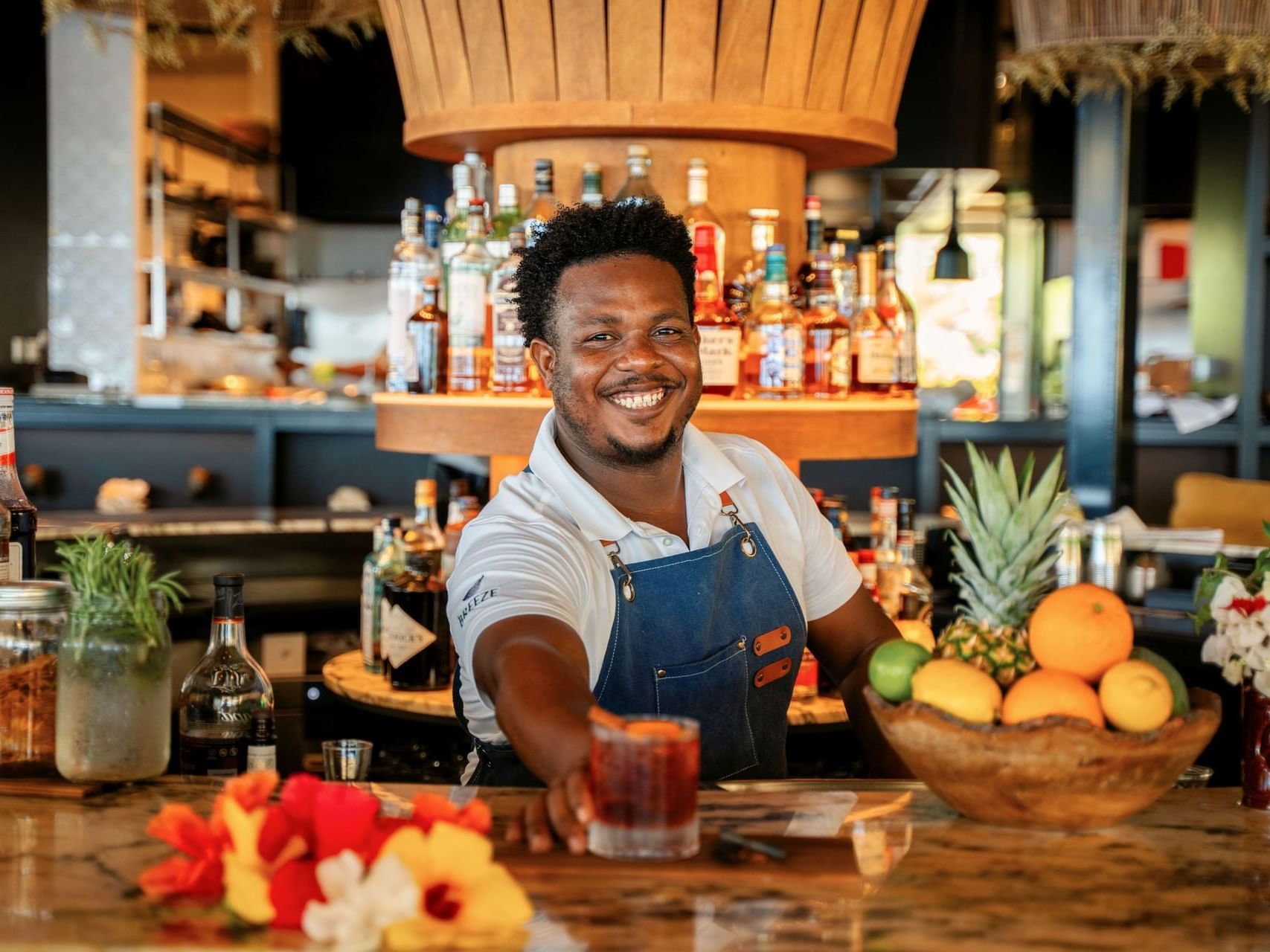 Bartender serving a cocktail at a vibrant bar with fresh fruits in the Breeze Restaurant at Golden Rock Resort