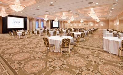 Grand ballroom with crystal chandeliers and round tables with white tablecloths set for event at Clayton Plaza Hotel