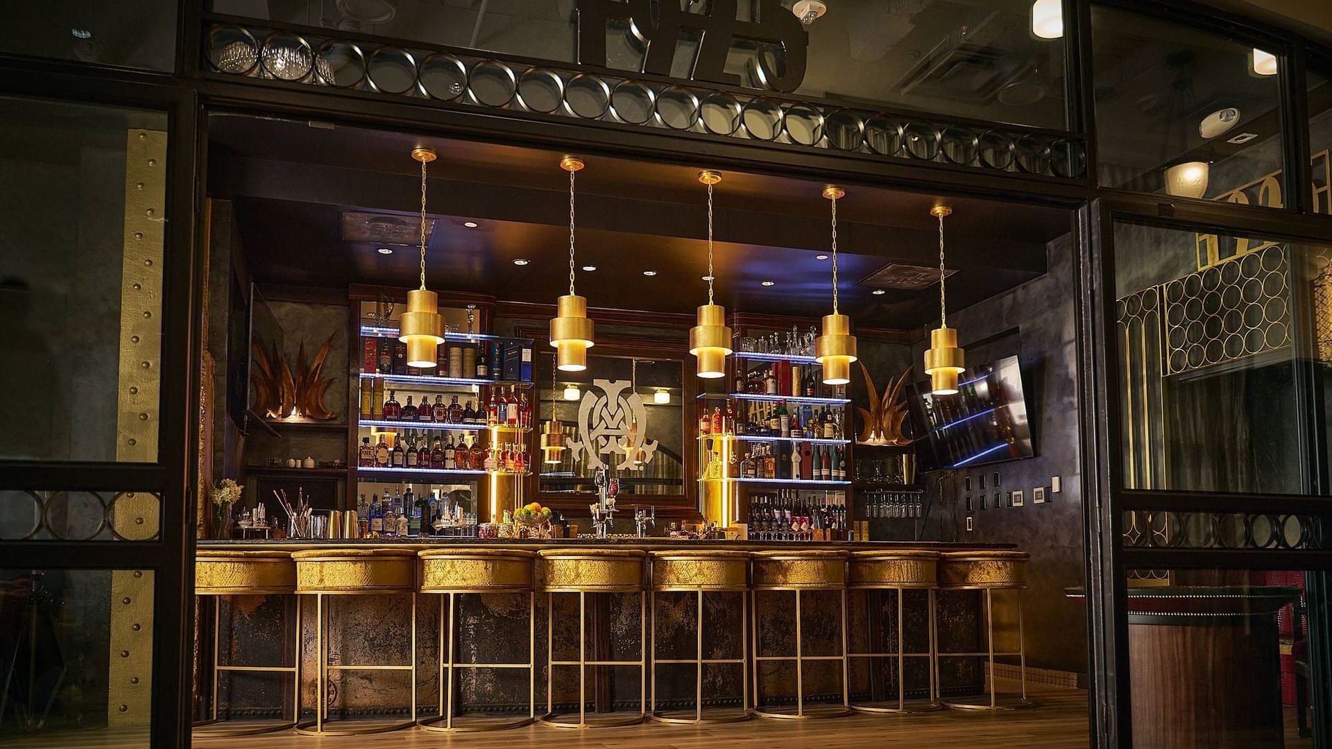 Bar interior with shelves full of bottles, golden stools, and a large entrance with the number 1923.