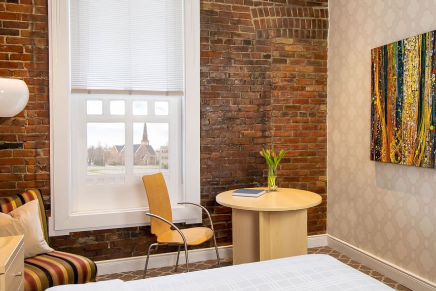 Work desk by the bed, window with blinds, comfy chair & brick wall in Queen Premiere Chardonnay at Retro Suites Hotel