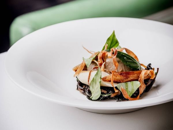 Plate with a dish of food garnished with greens and crispy elements at The Capital Hotel, Apartments & Townhouse - London.