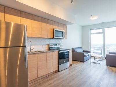 A view of a room with a sleek, full sized kitchen and sitting area with two couches close to large windows.