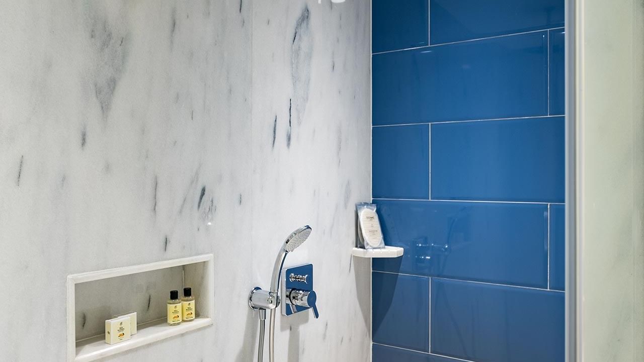 Modern shower with blue tiles, marble walls, built-in bench, showerhead, handheld shower, and luxury amenities at Titanic Luxury Collection Bodrum.