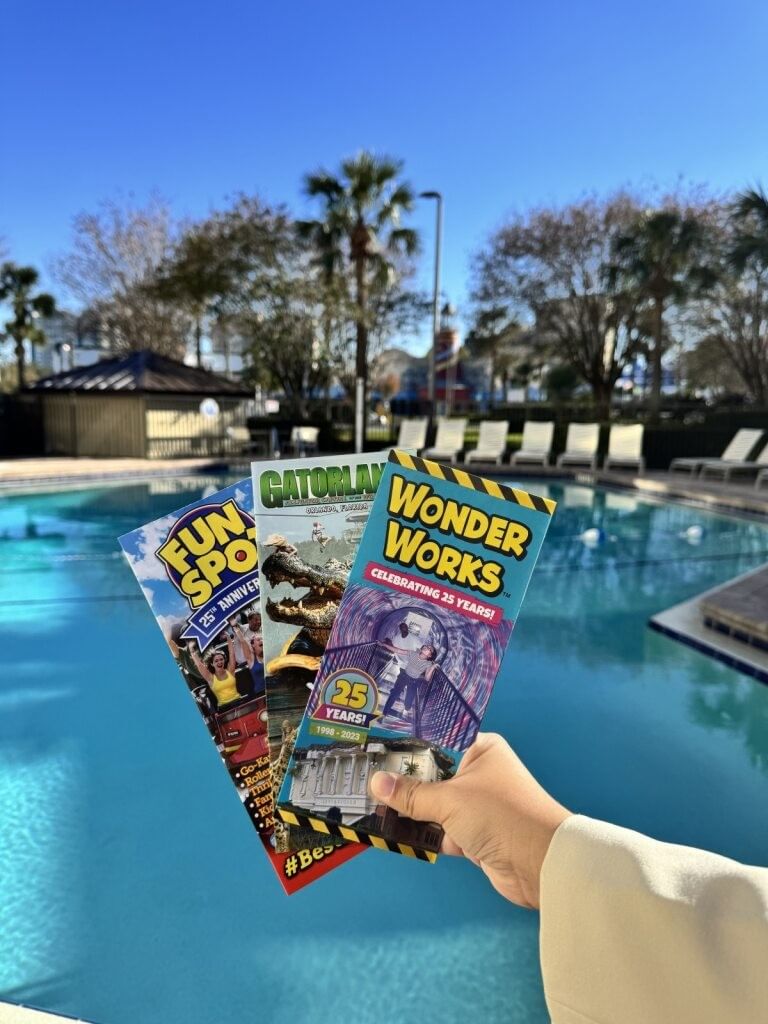 A hand holds brochures for Fun Spot, Gatorland, and Wonder Works in front of a pool. 