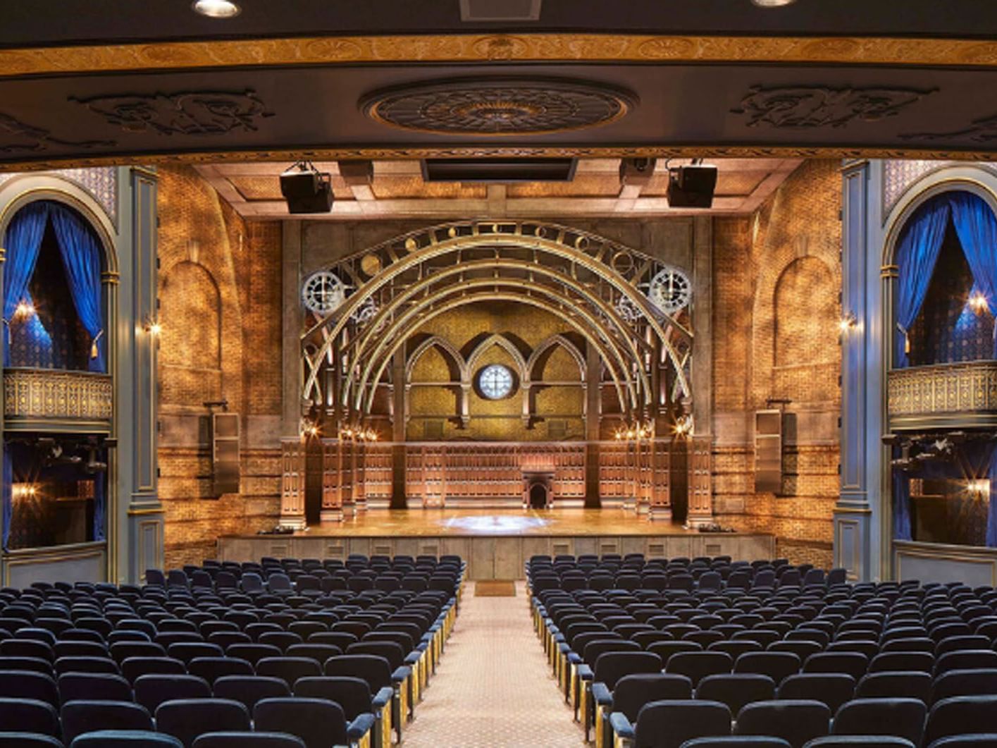 The Ed Mirvish Theatre with blue seats facing the stage with arches and a circular window near Hotel X Toronto