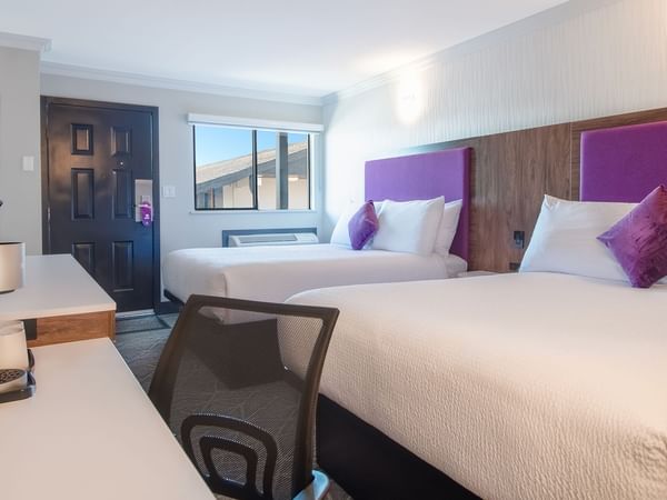 Hotel guestroom with two queen beds, work desk, TV, and coffee maker