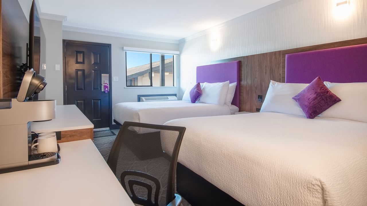 Hotel guestroom with two queen beds, work desk, TV, and coffee maker