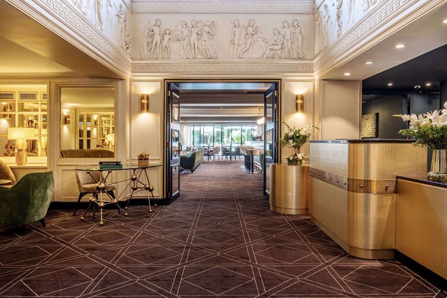 Patterned carpet hallway leading toward a sunlit restaurant and bar at Hotel Barsey by Warwick