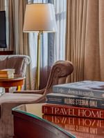 Stack of travel books on a glass table by velvet armchairs under a floor lamp in Deluxe King at Warwick Melrose Dallas
