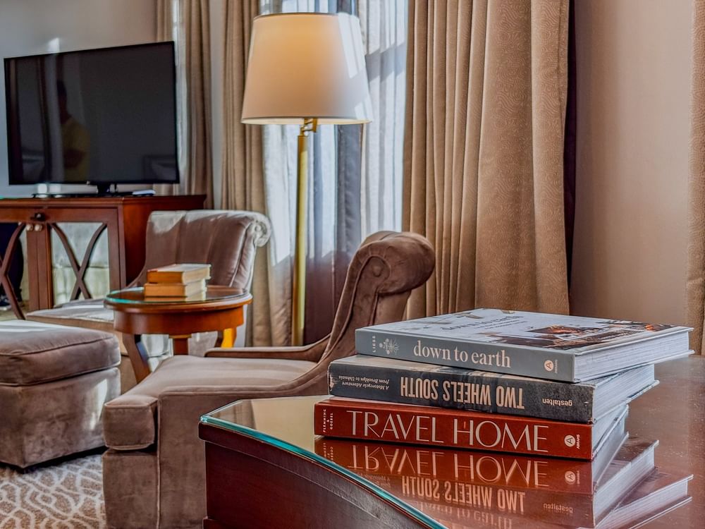 Stack of travel books on a glass table by velvet armchairs under a floor lamp in Deluxe Double at Warwick Melrose Dallas