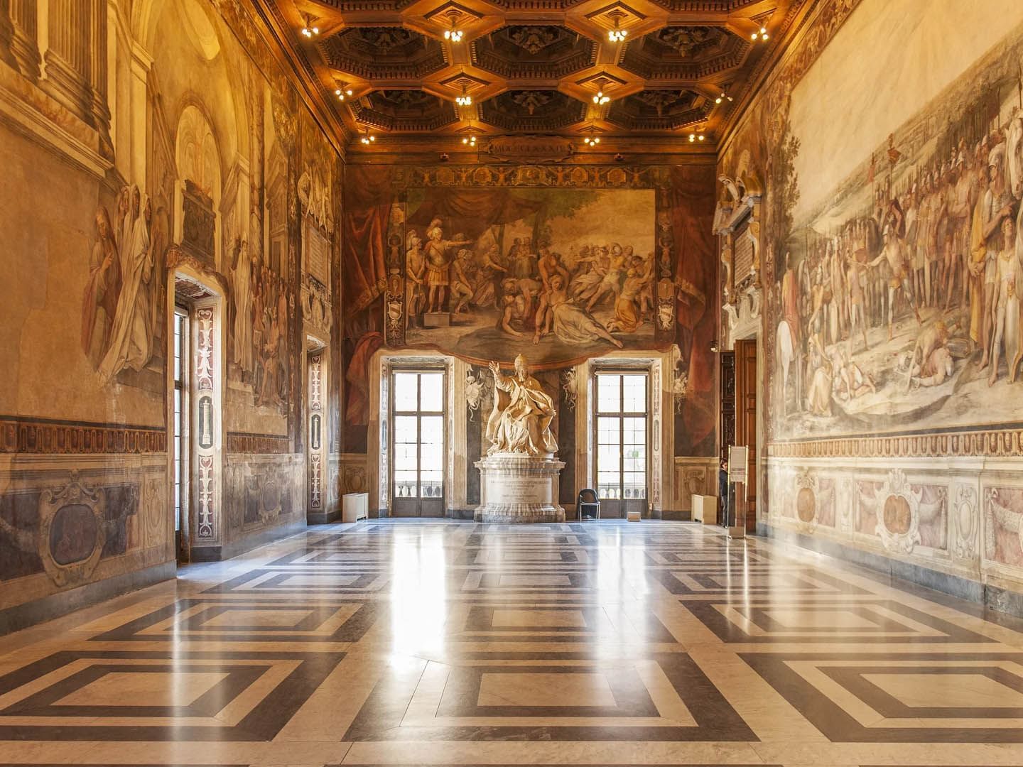 Interior of the Musei Capitolini featuring frescoes, a central statue, and intricate patterned flooring near The Glam Hotel
