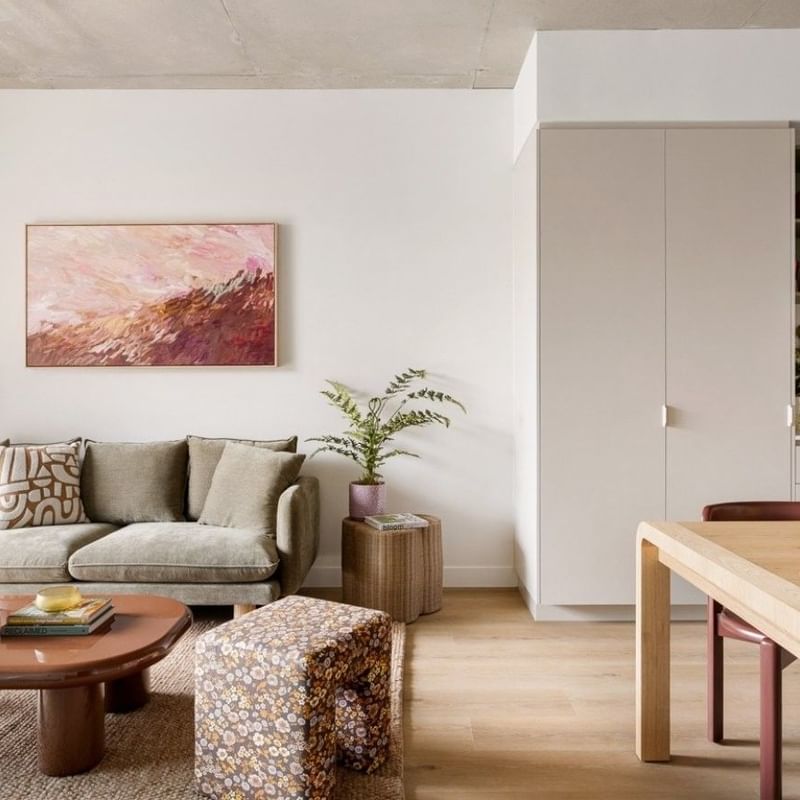 Modern open-plan living space with beige sofa, abstract artwork, wooden coffee table, and adjacent kitchen area.
