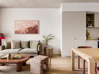 Modern open-plan living space with beige sofa, abstract artwork, wooden coffee table, and adjacent kitchen area.