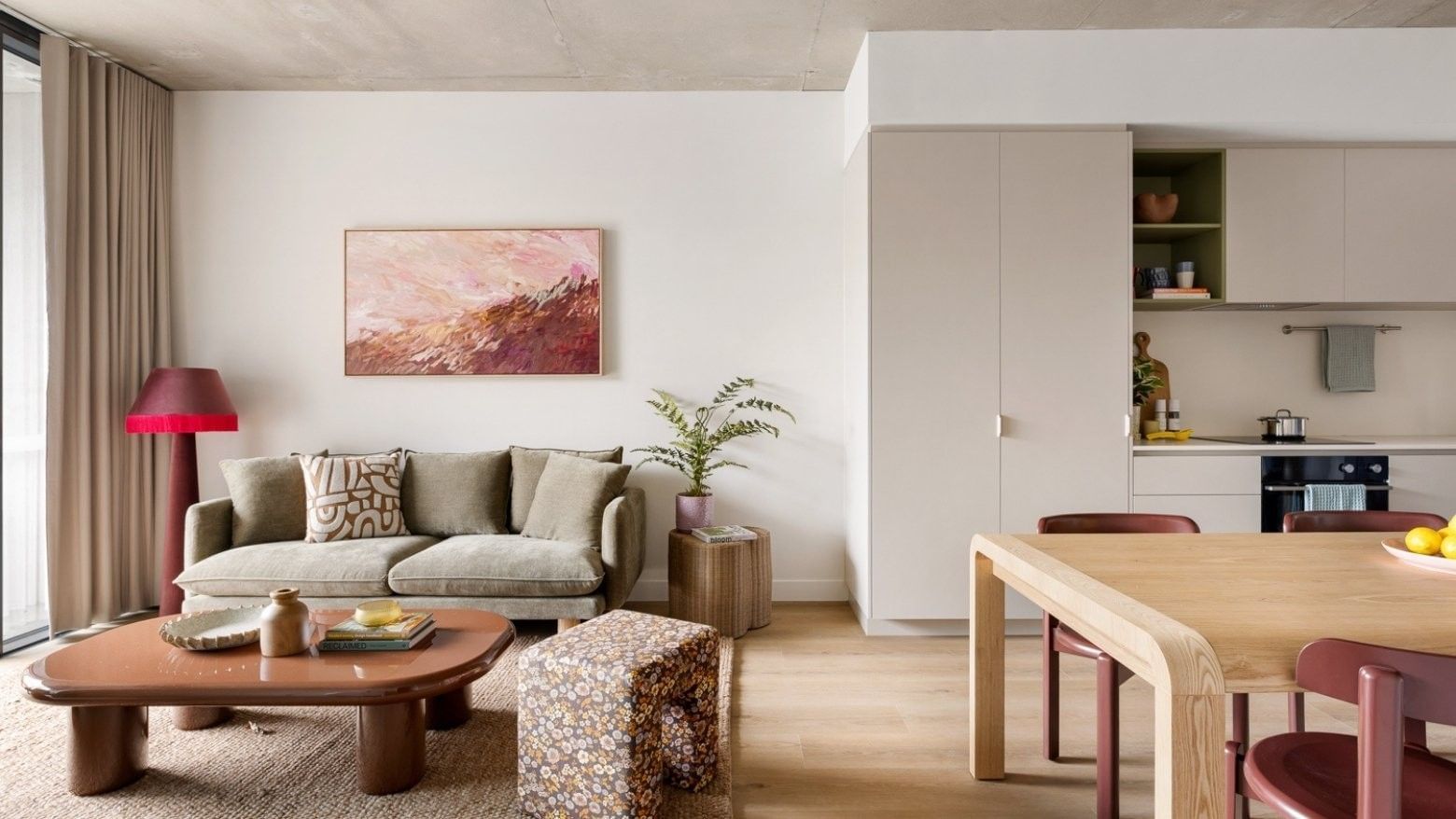 Modern open-plan living space with beige sofa, abstract artwork, wooden coffee table, and adjacent kitchen area.