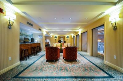Elegantly decorated business lounge with two red chairs, carpet, and a bar area with stools and computers.