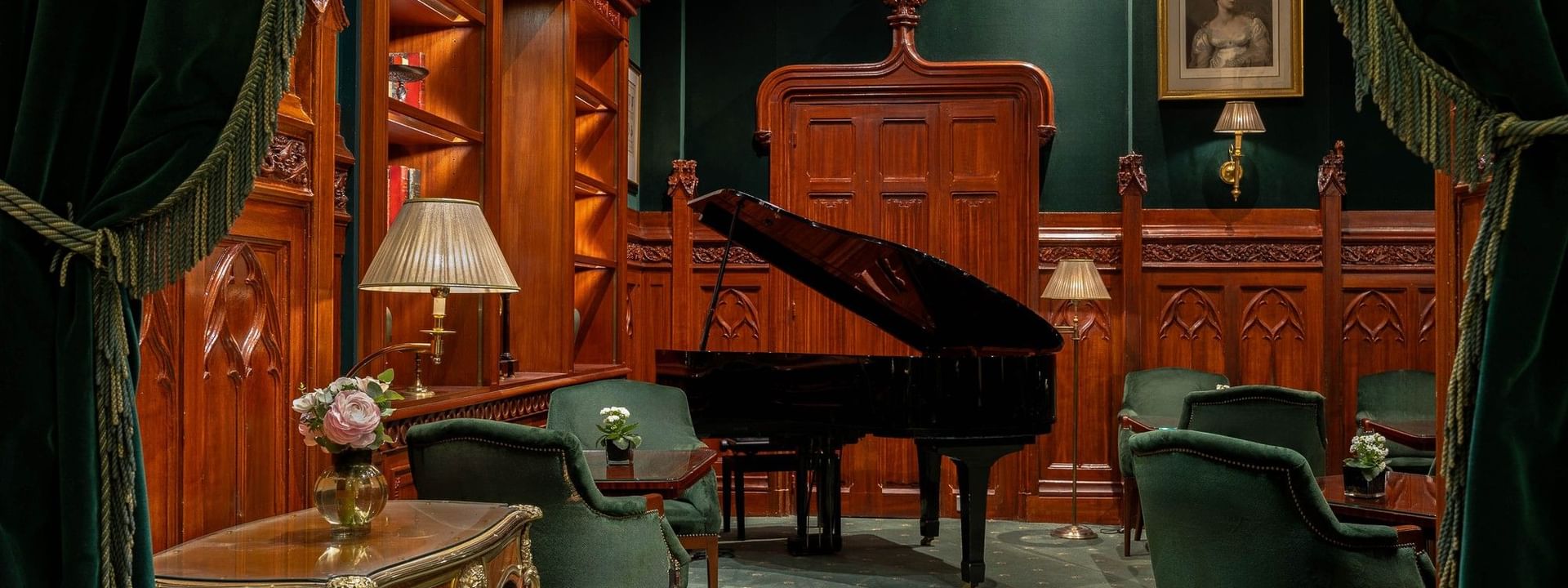 Black grand piano by velvet armchairs under a portrait and ornate wood paneling at Warwick Hotels & Resorts