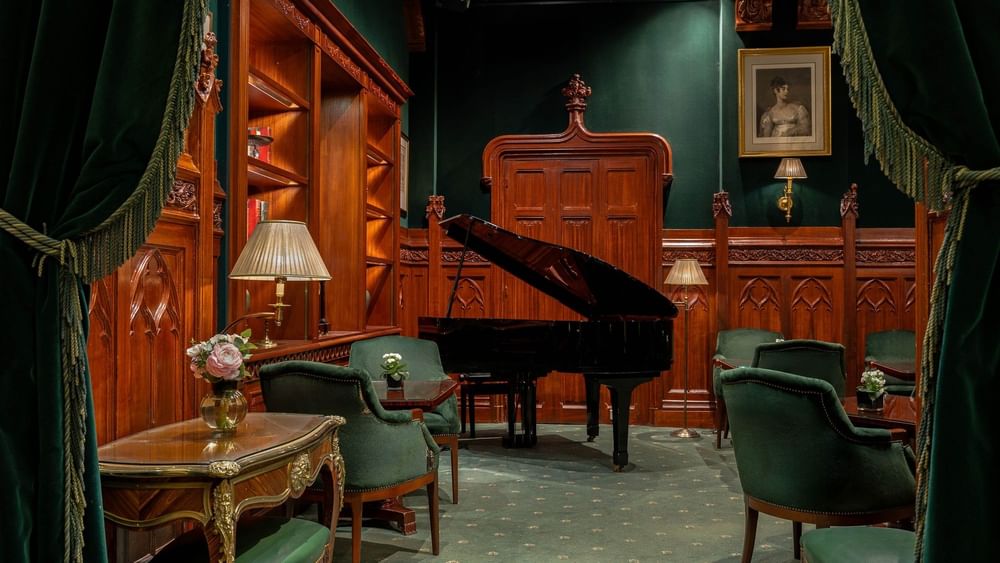 Black grand piano by velvet armchairs under a portrait and ornate wood paneling at Warwick Hotels & Resorts