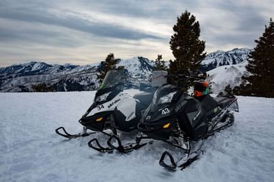 Two snowmobiles parking on snowy terrain with mountainous background near Hotel Park City Autograph Collection