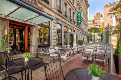 Outdoor patio seating with tables and chairs arranged along the brick sidewalk outside Harborside Inn Boston