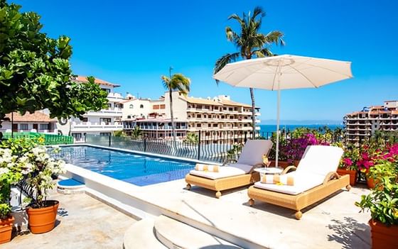Luxury rooftop swimming pool deck with comfortable lounge chairs and a white umbrella at Playa Los Arcos Beach Resort & Spa
