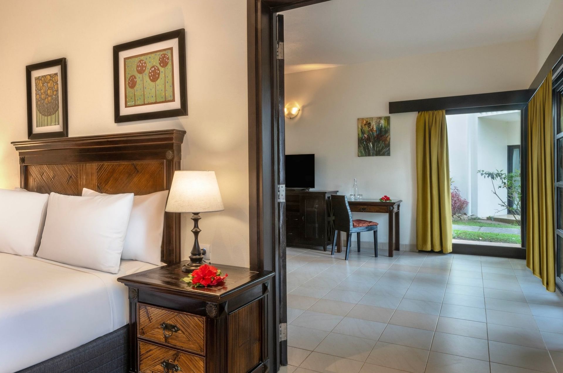 Wooden nightstand by a bed under a floral painting near a doorway in Suite at The Naviti Resort - Fiji