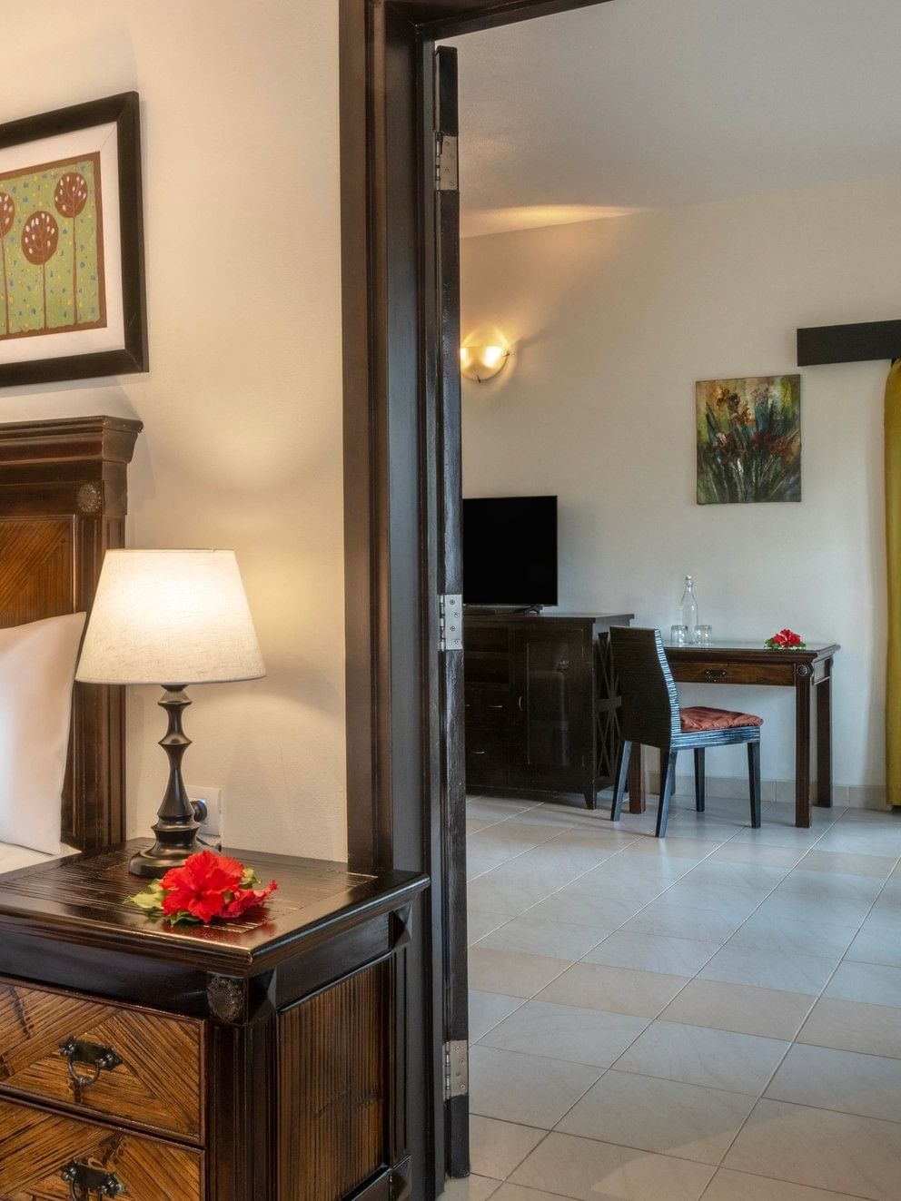 Wooden nightstand by a bed under a floral painting near a doorway in Suite at The Naviti Resort - Fiji