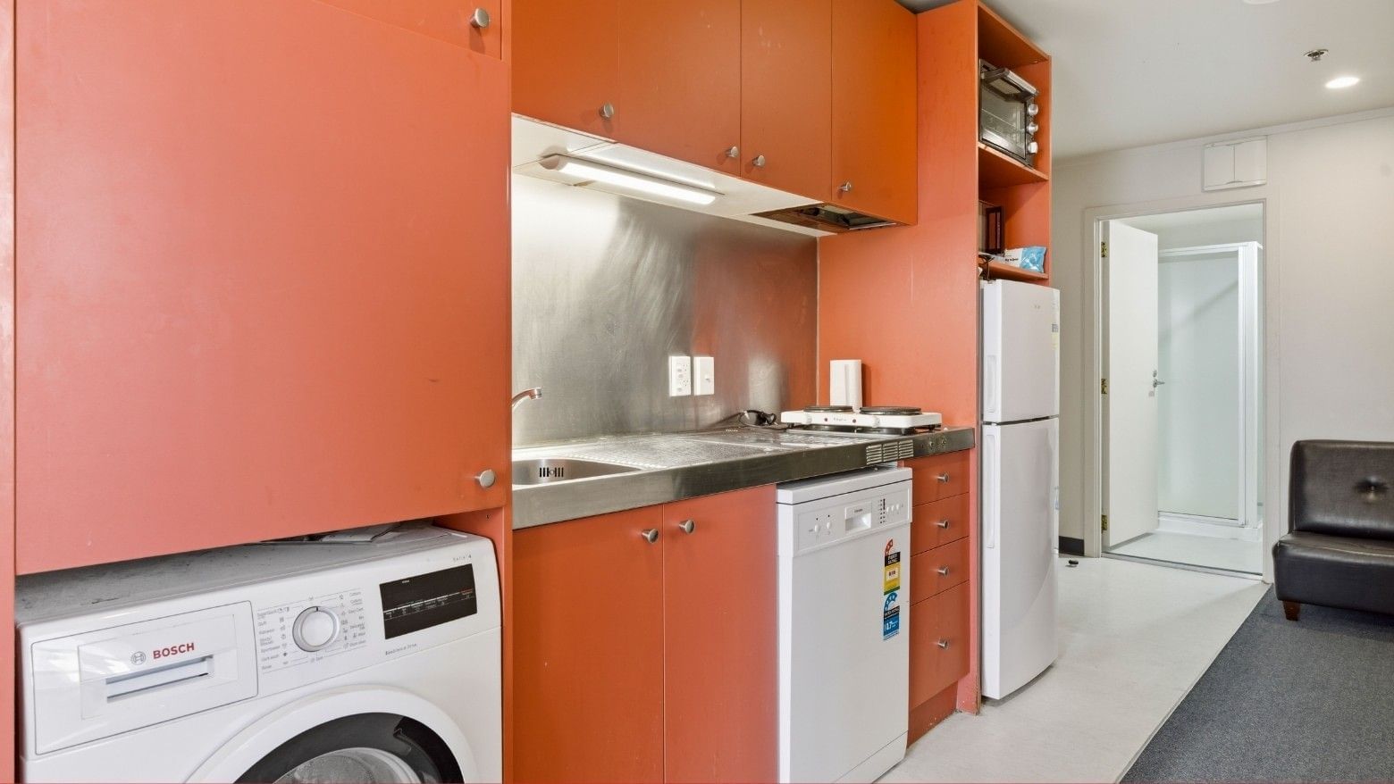 Orange cabinets with integrated appliances in a modern kitchen at UniLodge Stafford House.