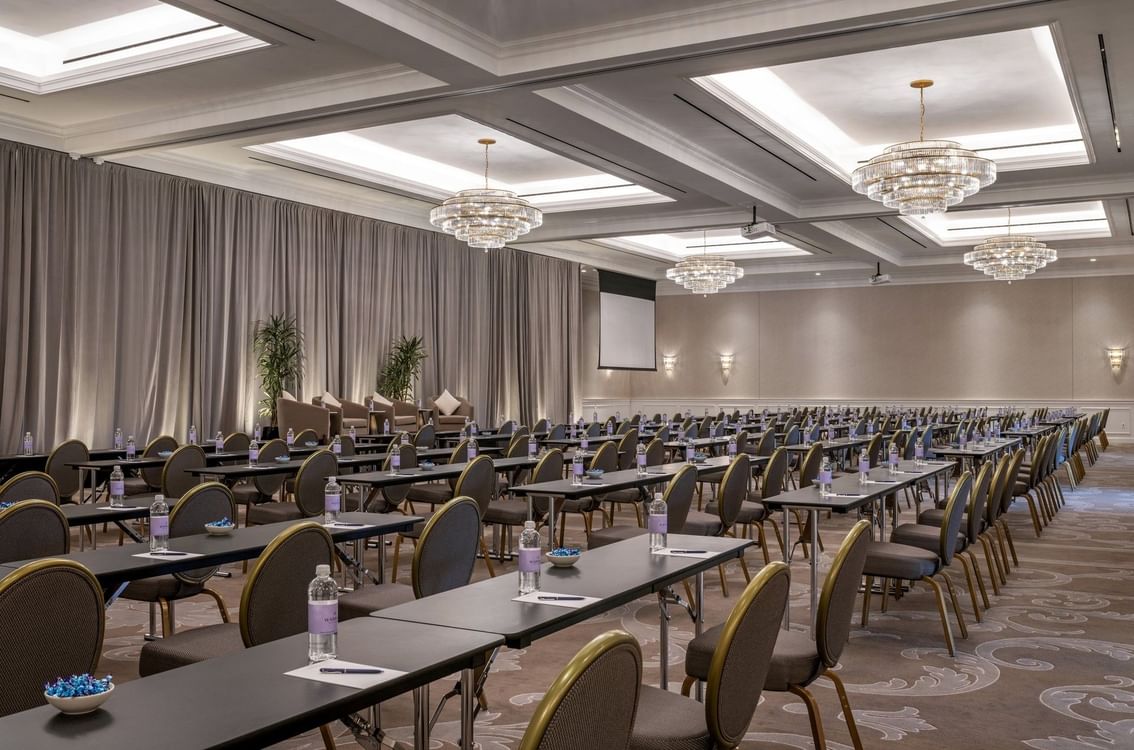 Classroom tables by water bottles under crystal chandeliers in Turtle Creek Ballroom C at Warwick Melrose Dallas