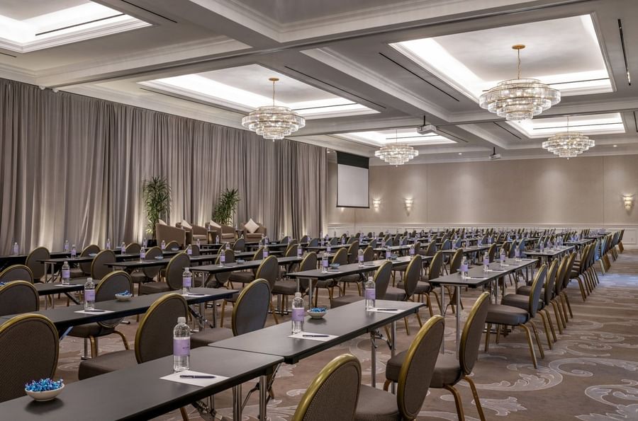 Classroom tables by water bottles under crystal chandeliers in Turtle Creek Ballroom C at Warwick Melrose Dallas