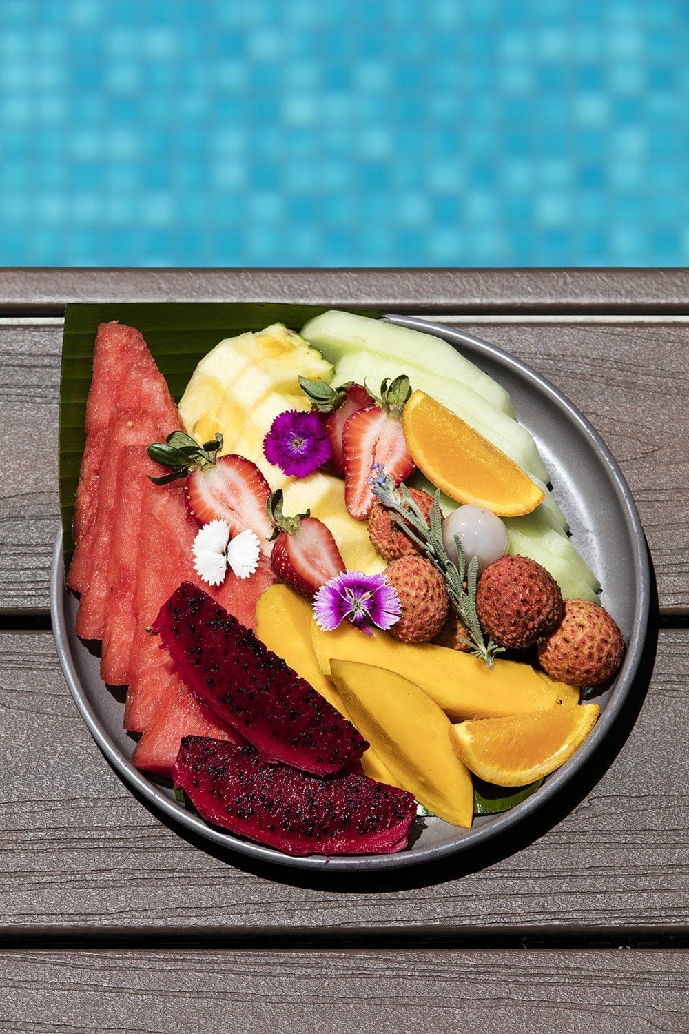 A tropical fruit platter with dragon fruit, lychee, and mango on a wooden deck by the pool at The Sebel Brisbane