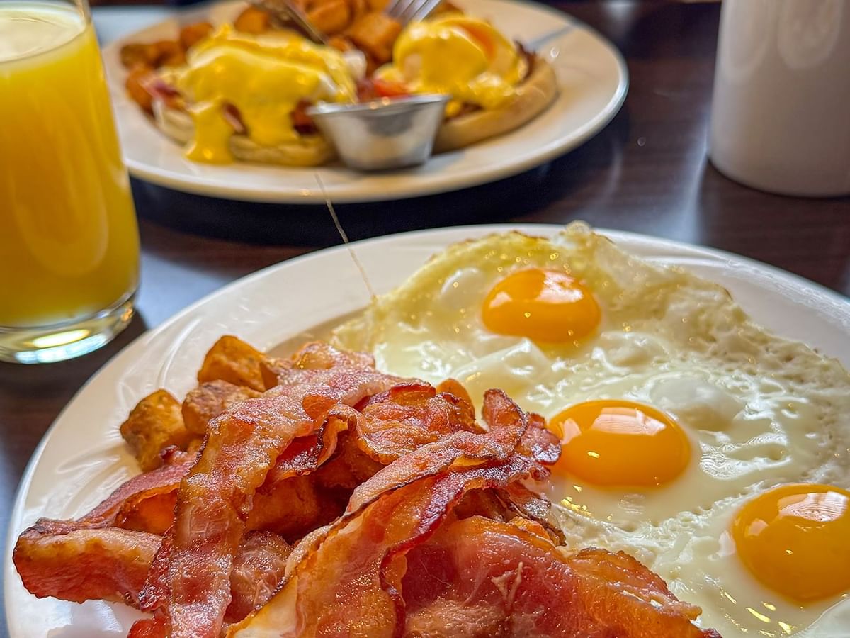 Two plates with eggs, bacon, and a glass of orange juice on a table.