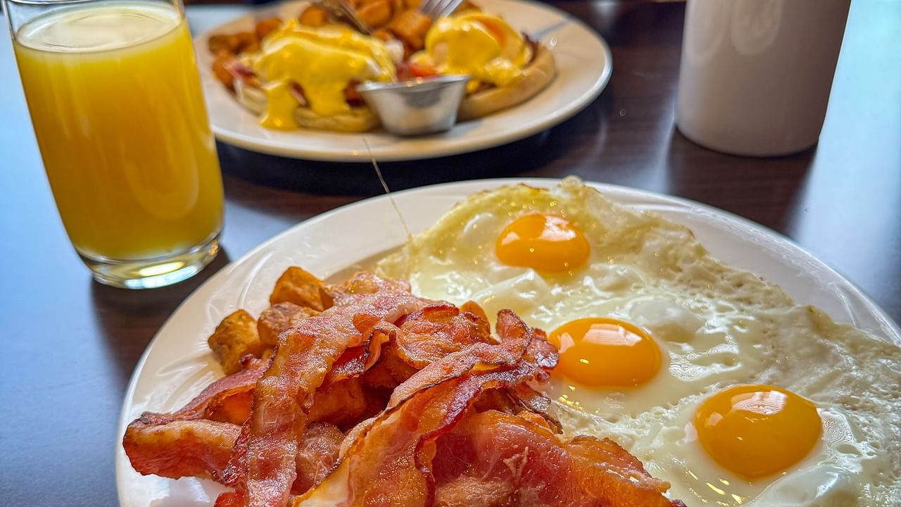 Two plates with eggs, bacon, and a glass of orange juice on a table.