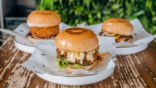 Three burgers on white plates with a green plant background served at The Sebel Auckland Viaduct Harbour