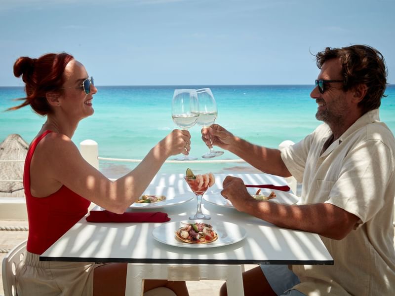 Couple celebrating with wine glasses at a table with beach view at Fiesta Americana