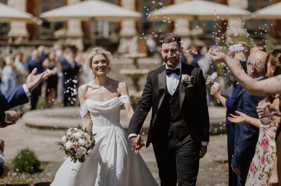Newlyweds walking through confetti outside the Mansion House at Easthampstead Park
