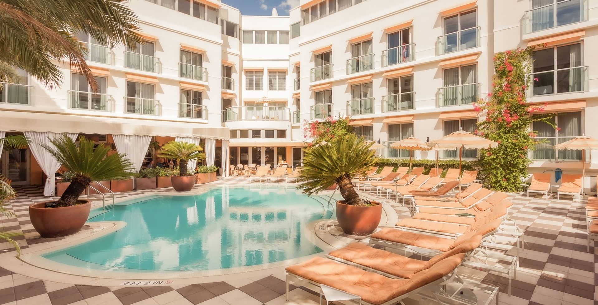 A pool area with lounge chairs, palm trees, and a hotel building in the background.