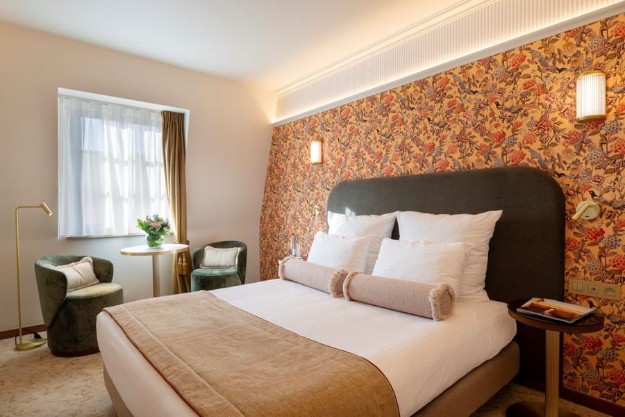 Elegant hotel room with floral wallpaper, plush bed, seating area, and modern lighting at Warwick Brussels Grand-Place