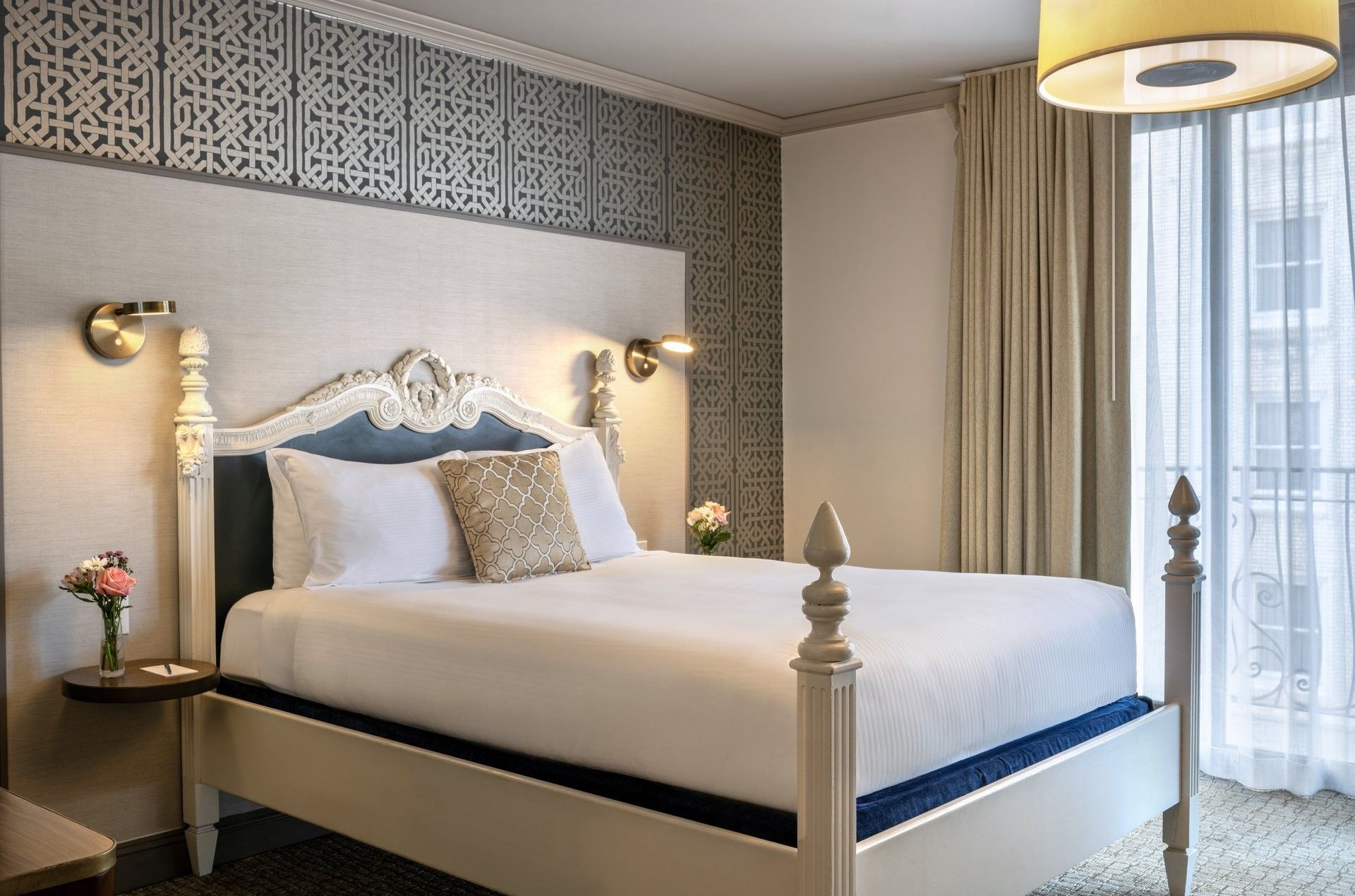 Classic bed by tan curtains and a geometric wall under soft lighting in Balcony Suite at Warwick San Francisco