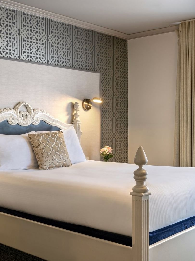 Classic bed by tan curtains and a geometric wall under soft lighting in Balcony Suite at Warwick San Francisco