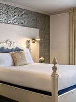 Classic bed by tan curtains and a geometric wall under soft lighting in Balcony Suite at Warwick San Francisco